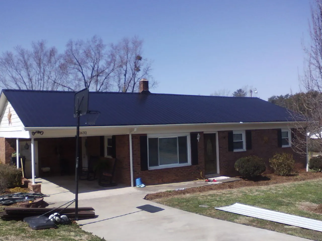 Finished dark blue metal roof on a brick ranch with a carport in Moodus