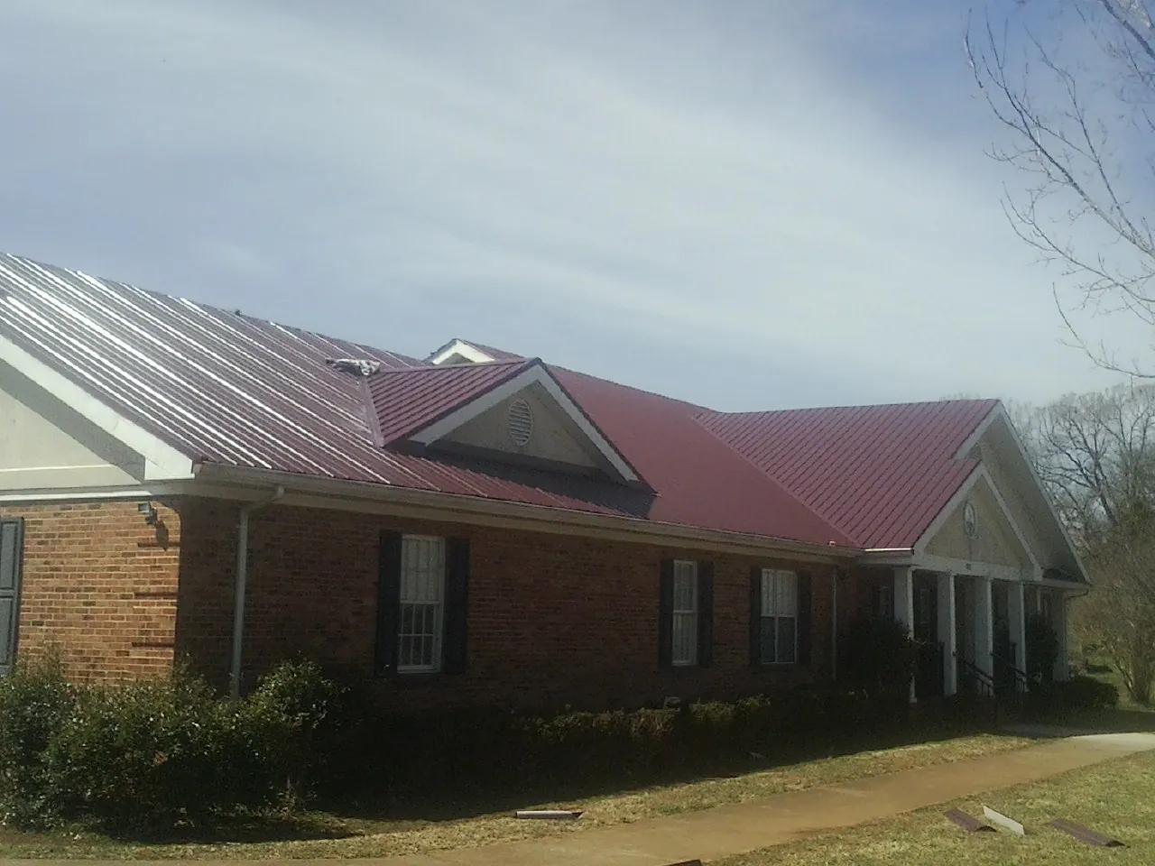 Red metal roof with gabled entries on a long brick building, from a Hail Damage Roof Repair job in Moodus