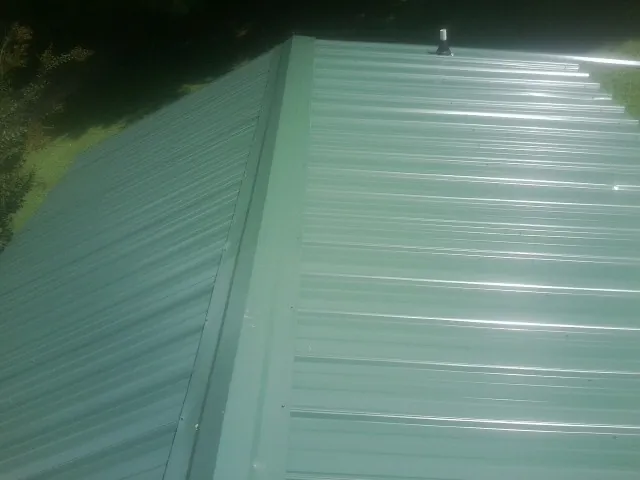 New green metal panels meeting at the ridge of a roof — Flat Roof Repair work by our crew in Moodus