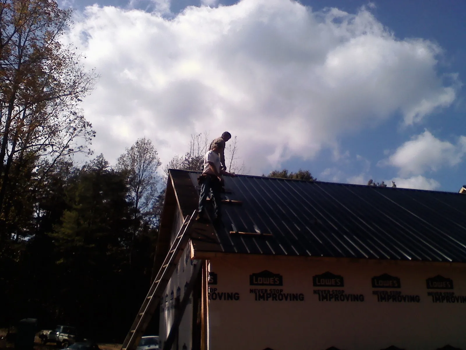 Roofer fastening dark metal panels high against a cloudy sky, from a Roof Inspection job in Moodus